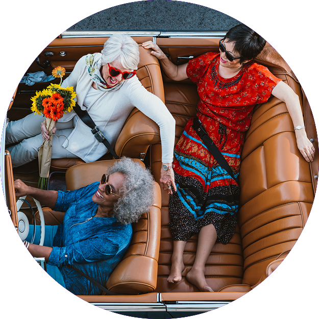 Three older women driving and talking in a convertible car
