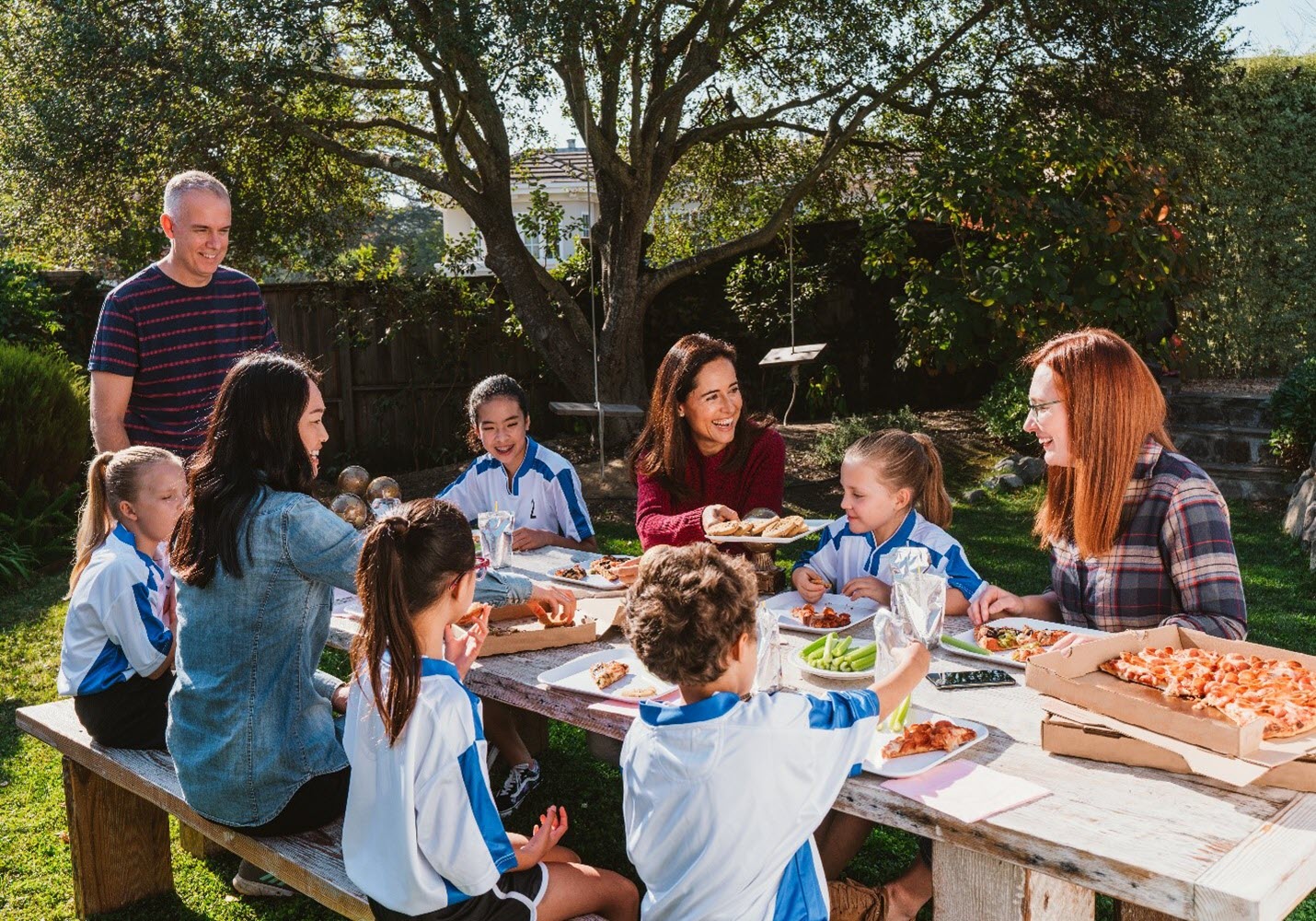parents and kids gather around picnic table for pizza party